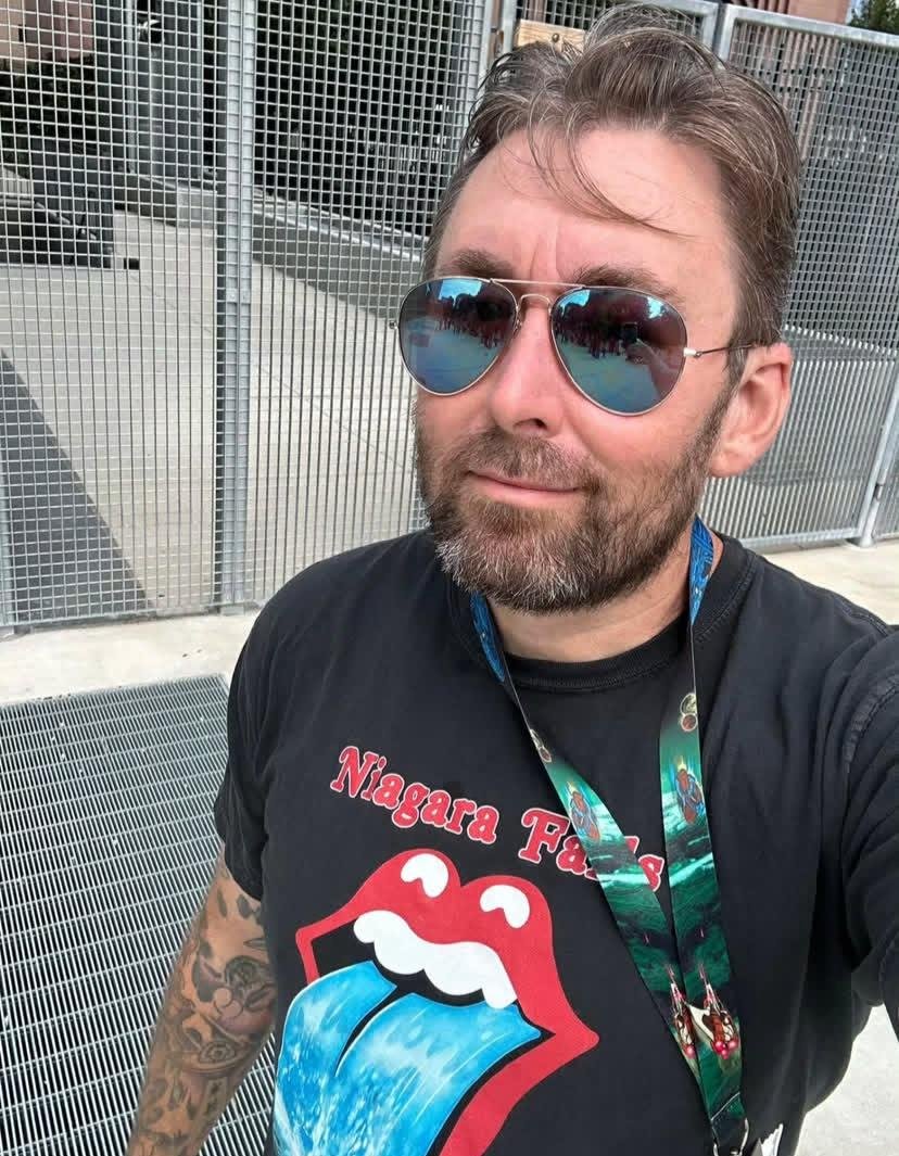 A warm, mid distance portrait of Adam the Woo outdoors, casual clothes, camera in hand